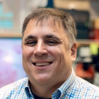 Brian Summa smiling, in a blue checked shirt, in a lab.